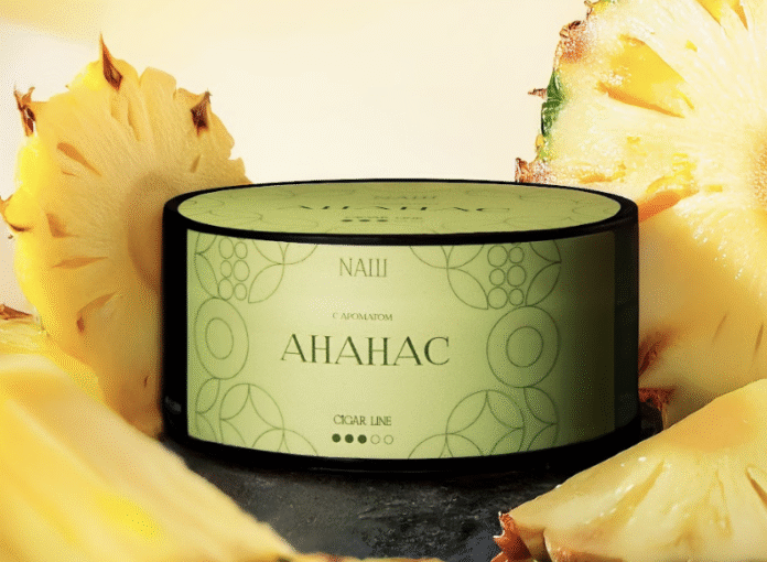 טבק לנרגילה Nash Cigar Line בטעם אננס – תמונת מוצר עם אננסים קופסת טבק לנרגילה Nash Cigar Line בטעם אננס ליד פרוסות אננס טרי